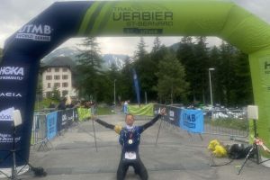 UTMB Verbier arrivo TRM Team MArco Mori inginocchiato sotto il gonfalone dellarrivo scaled e1725980552426 24b6905f