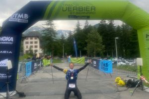 UTMB Verbier arrivo TRM Team MArco Mori inginocchiato sotto il gonfalone dellarrivo scaled e1725980552426 fd4cd8ad