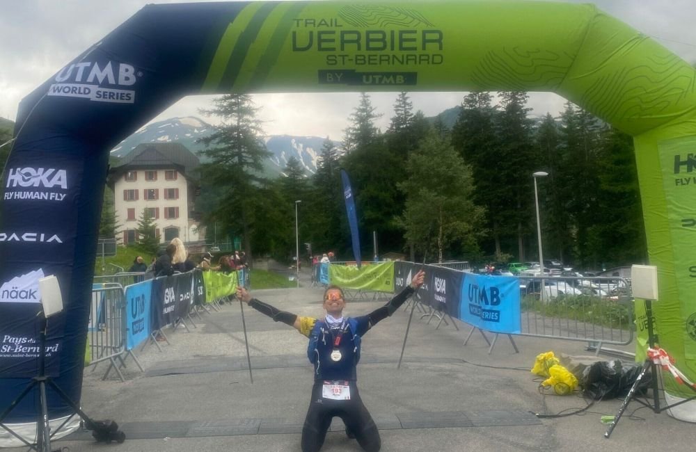 UTMB Verbier arrivo TRM Team MArco Mori inginocchiato sotto il gonfalone dellarrivo scaled e1725980552426 ce788c0c
